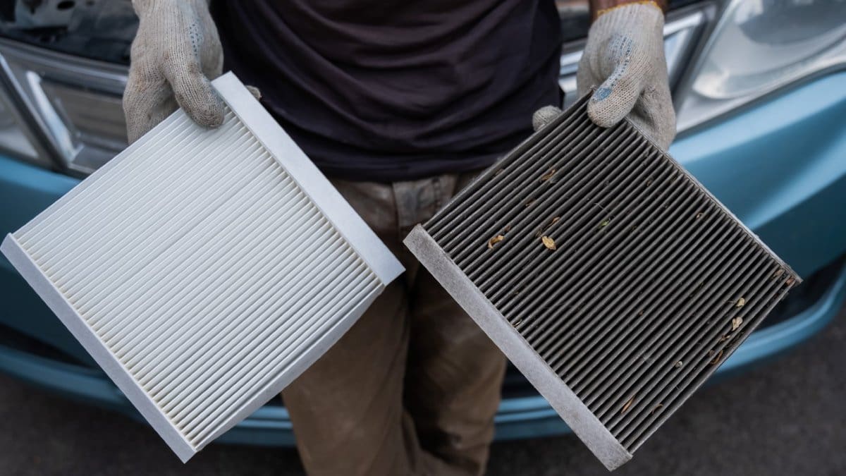 A technician holding a clean cabin air filter beside a dirty one removed from a vehicle