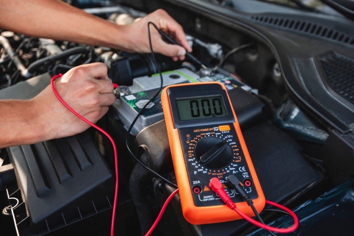 Technician testing a car battery with a multimeter under the hood