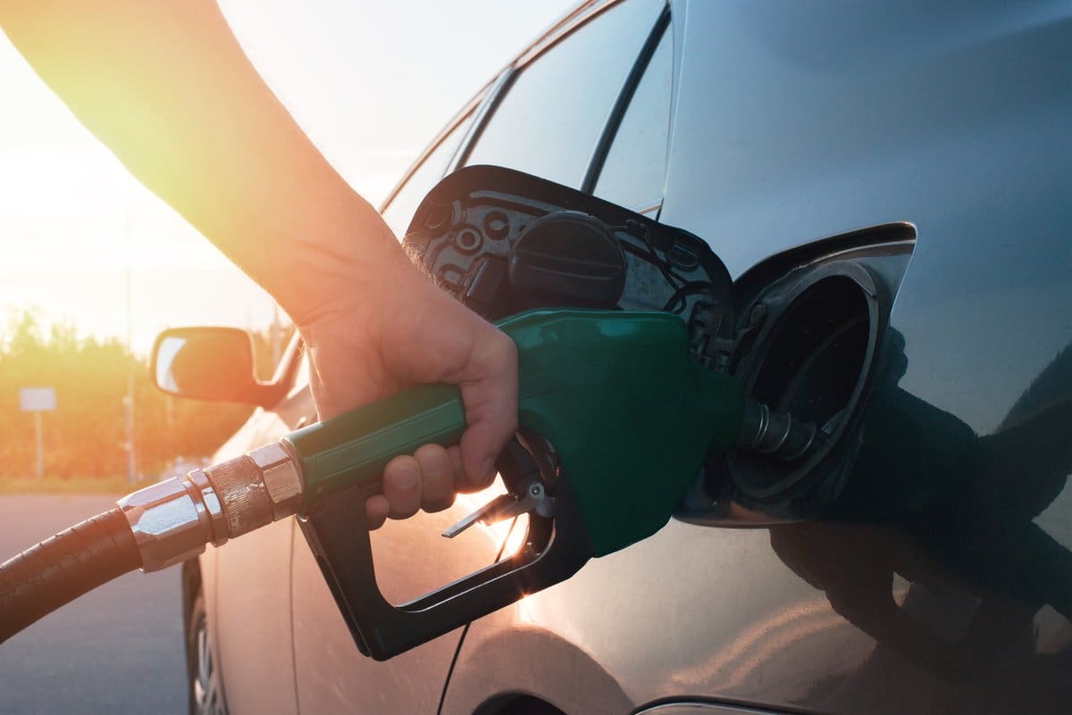 Driver filling a vehicle's fuel tank at a gas station on a sunny day