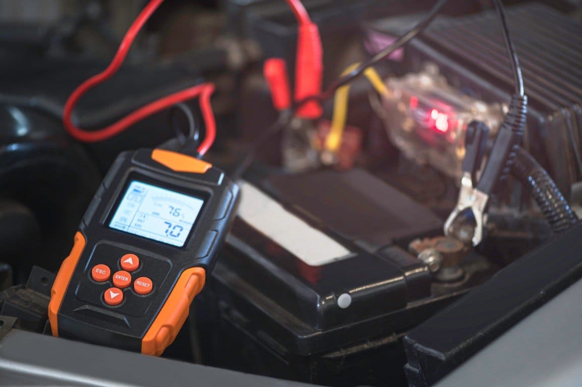 Digital battery tester connected to a car battery during a charging system check