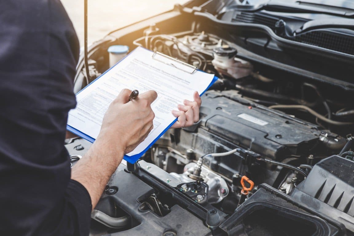 Technician completing a vehicle inspection checklist at an open engine bay