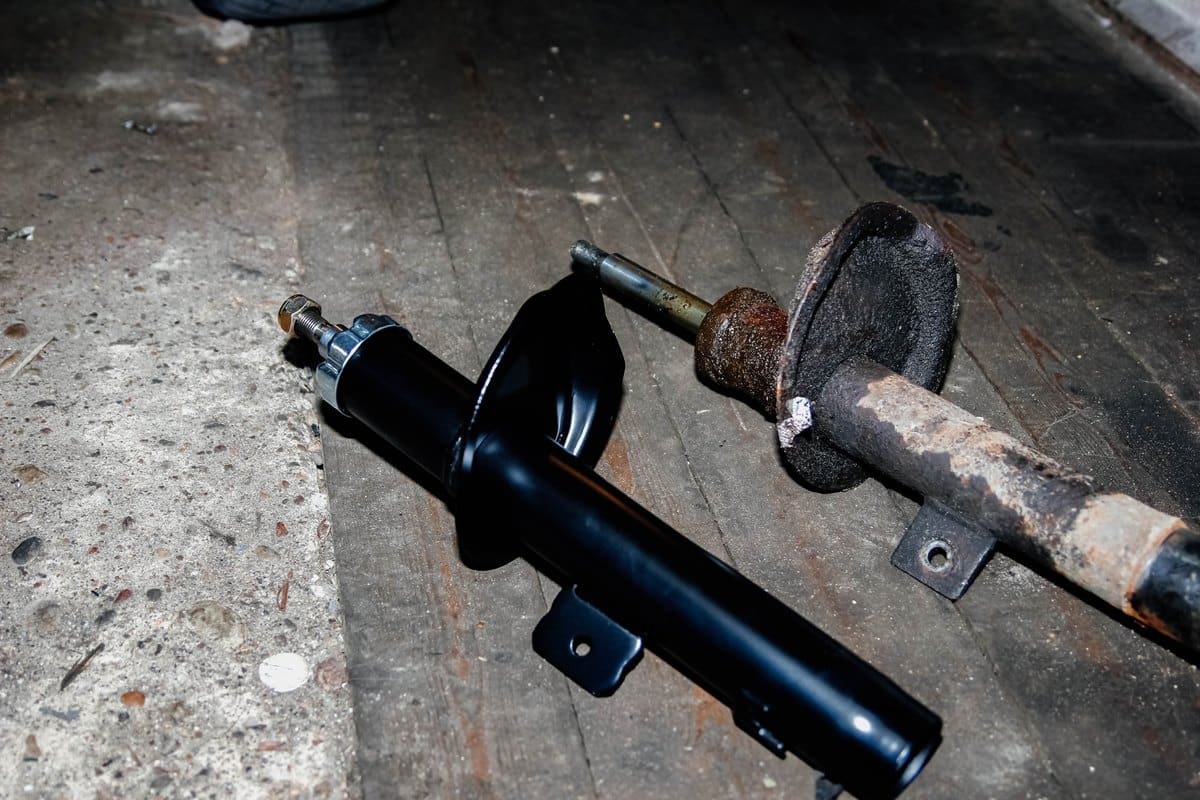 Technician holding a replacement strut and coil spring assembly in a workshop