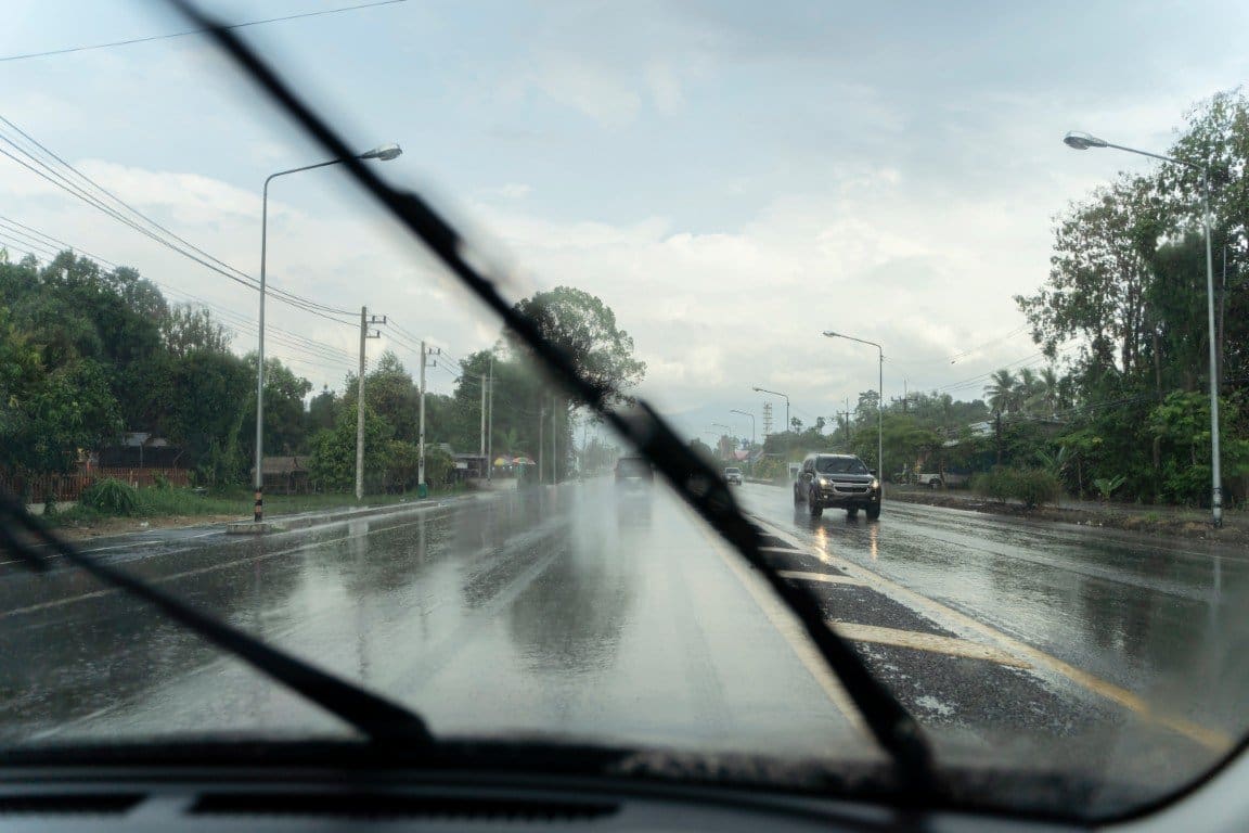 View through a windshield with wipers clearing heavy rain on a wet Tennessee road